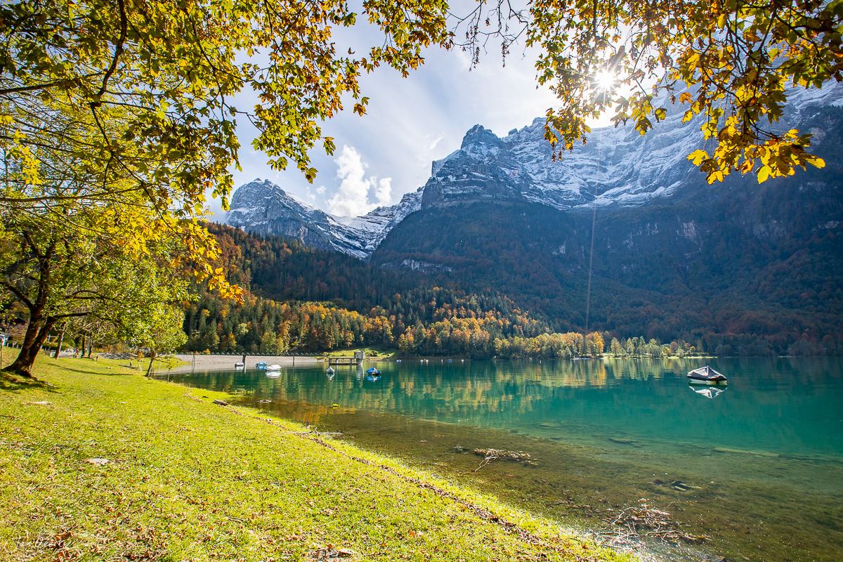 Herbstlich gefärbter Bergsee Klöntalersee mit schneebedeckten Alpen, leuchtend gelbe Lärchen und türkises Wasser in der Schweiz – Jan Geerk Fotograf Basel