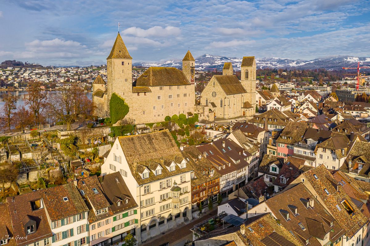Schloss Rapperswil mit Kirche und Altstadt in Kantlicht, schneebedeckte Alpen im Hintergrund, Schweiz – Jan Geerk Fotograf Basel