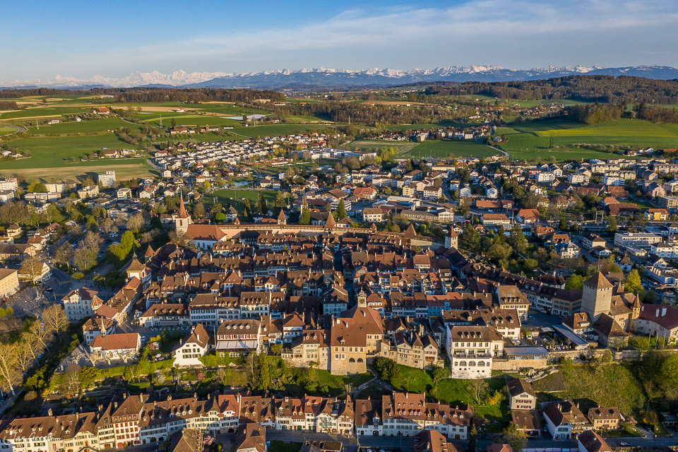 Luftaufnahme von Murten mit Alpen im Hintergrund, Frühlingslicht, Seeland Schweiz – Jan Geerk Fotograf Basel