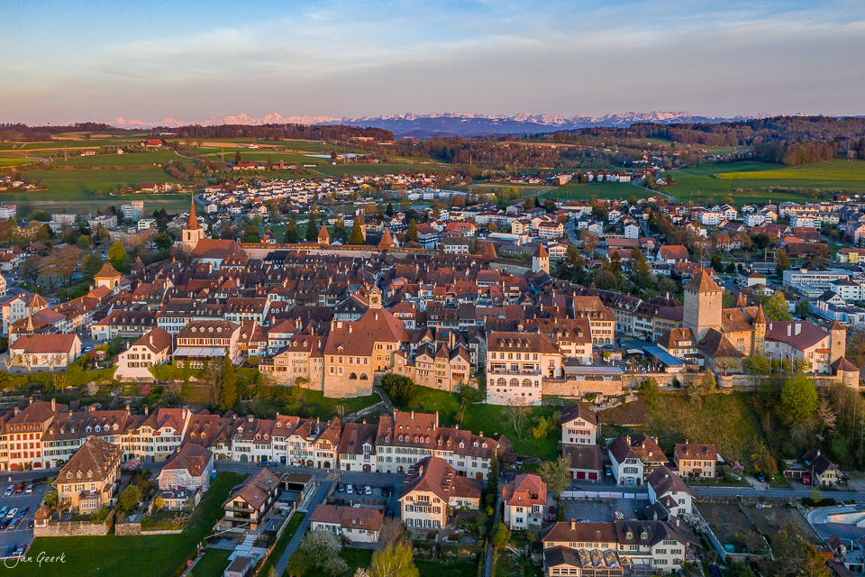 Luftaufnahme von Murten mit mittelalterlicher Altstadt, Alpen im Hintergrund, Frühlingslicht, Seeland, Schweiz – Jan Geerk Fotograf Basel