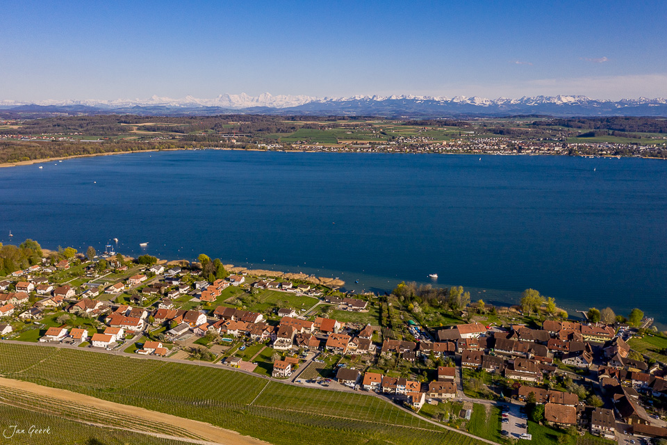 Luftaufnahme des Murtensee mit Dorf Praz, Alpen im Hintergrund, Frühling, Seeland Schweiz – Jan Geerk Fotograf Basel