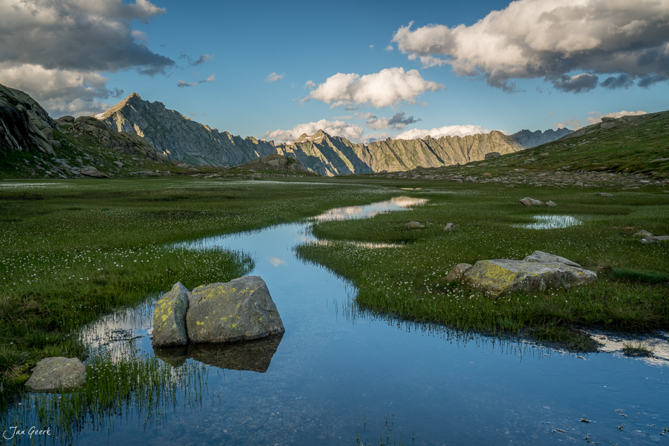 Alpensee mit Steinen, Lajozz Hochebene, grüne Wiesen und dramatische Berggipfel bei Sonnenschein, Tessin Schweiz – Jan Geerk Fotograf Basel