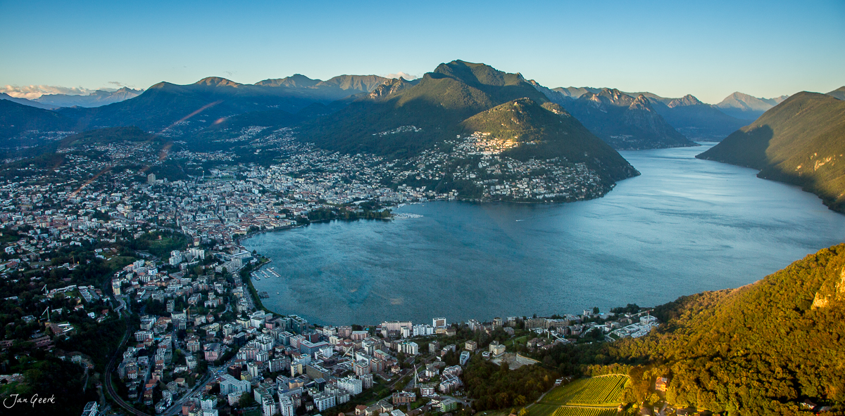 Lugano Luftaufnahme mit türkisfarbenem See, umgeben von Bergen und Stadt im goldenen Herbstlicht, Tessin Schweiz – Jan Geerk Fotograf Basel