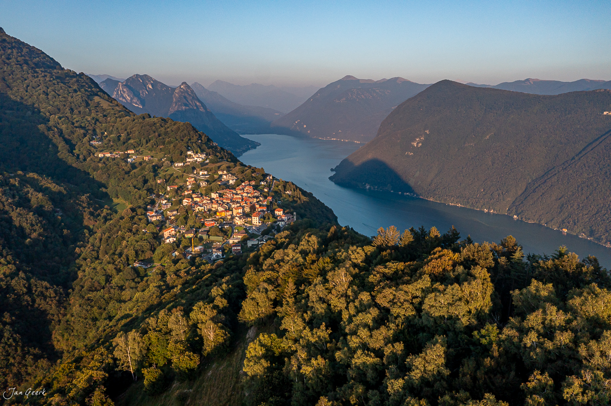 Luftaufnahme Lugano mit See, umliegenden Bergen und herbstlichem Wald bei Kantlicht Schweiz – Jan Geerk Fotograf Basel