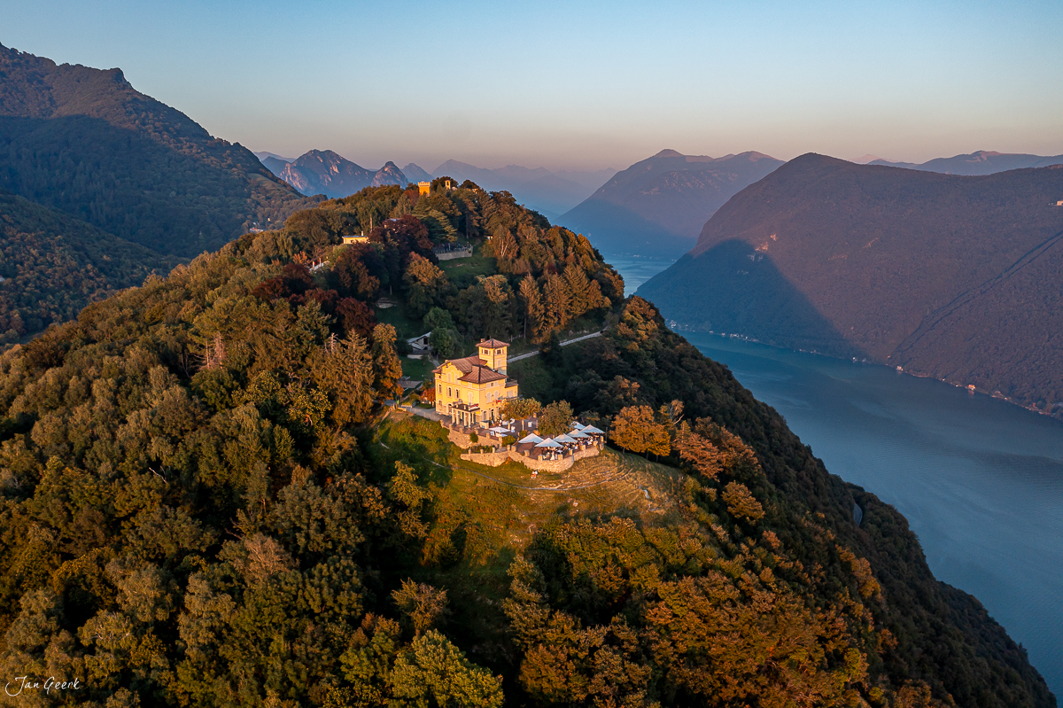 Luftaufnahme Lugano mit Kirche auf Bergspitze, herbstliche Wälder, blaues Seepanorama, Tessin Schweiz – Jan Geerk Fotograf Basel