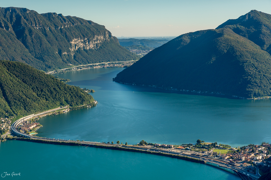 Luftaufnahme Lugano mit türkisblauem See, bewaldeten Bergen und Uferpromenade bei Sonnenschein, Tessin Schweiz – Jan Geerk Fotograf Basel
