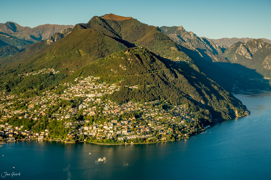 Luftaufnahme Lugano mit Bergen, Seeufer und Siedlung in Sommerlicht, Tessin Schweiz – Jan Geerk Fotograf Basel