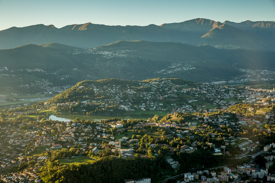 Luftaufnahme von Lugano mit Fluss, Seen und Bergen im Gegenlicht, Herbststimmung Tessin Schweiz – Jan Geerk Fotograf Basel