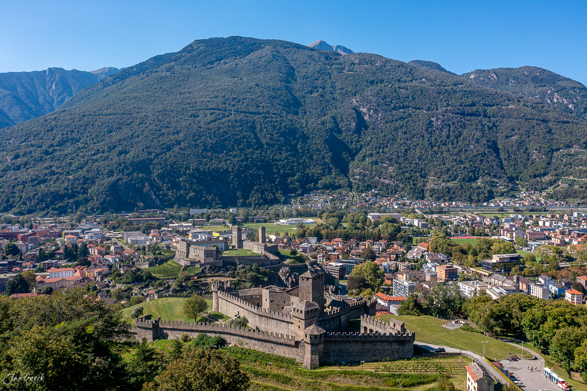 Mittelalterliche Burganlage mit Stadtpanorama und bewaldeten Bergen unter blauem Himmel Schweiz – Jan Geerk Fotograf Basel