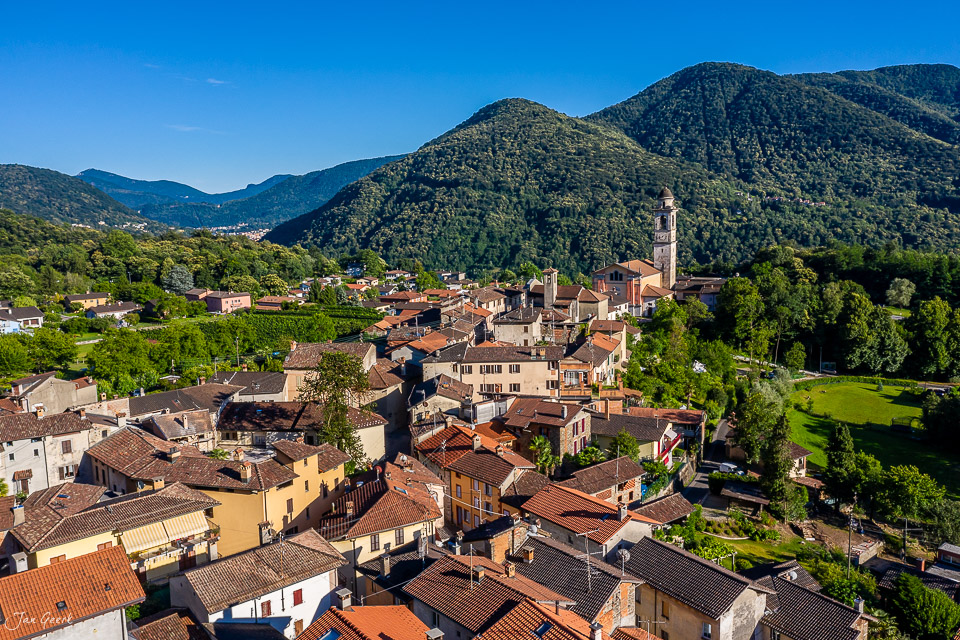 Luftaufnahme des Dorfes Sessa mit Kirche, umgeben von grünen Bergen im Tessin, Schweiz – Jan Geerk Fotograf Basel