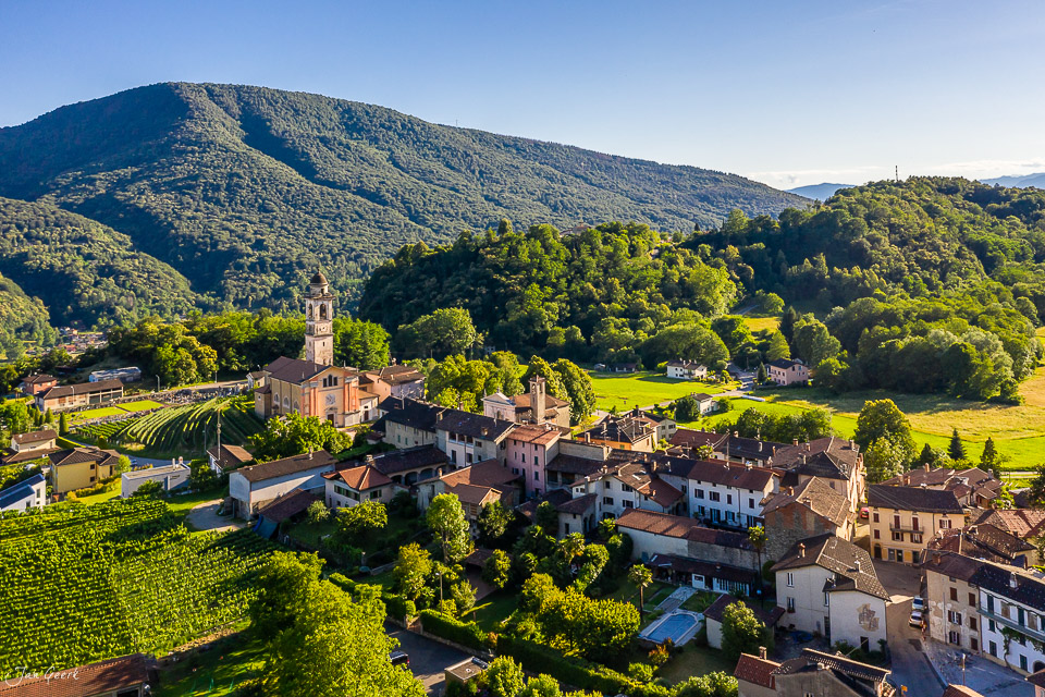 Luftaufnahme des Dorfes Sessa mit Kirche, umgeben von grünen Hügeln und Wäldern im Tessin Schweiz – Jan Geerk Fotograf Basel