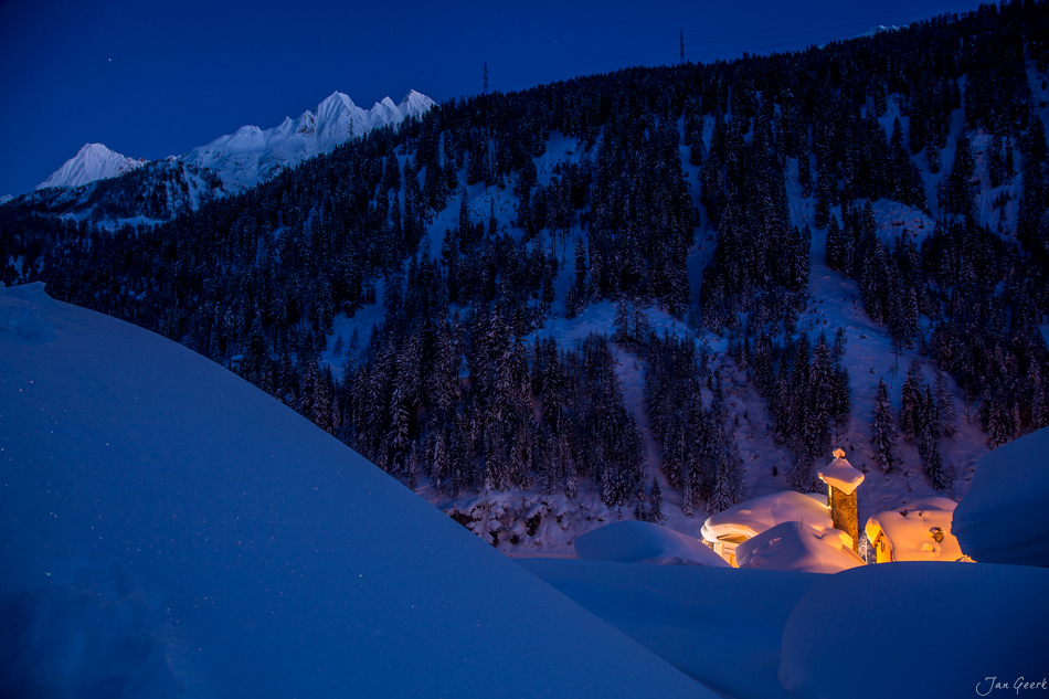 Beleuchtete Kapelle in schneebedeckter Winterlandschaft Bedretto mit verschneiten Südalpen Tessin Schweiz – Jan Geerk Fotograf Basel