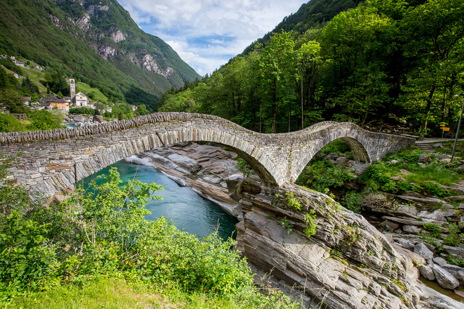 Historische Steinbogenbrücke über türkisfarbenen Bach im Bleniotal, grüne Berglandschaft, Frühling, Tessin Schweiz – Jan Geerk Fotograf Basel