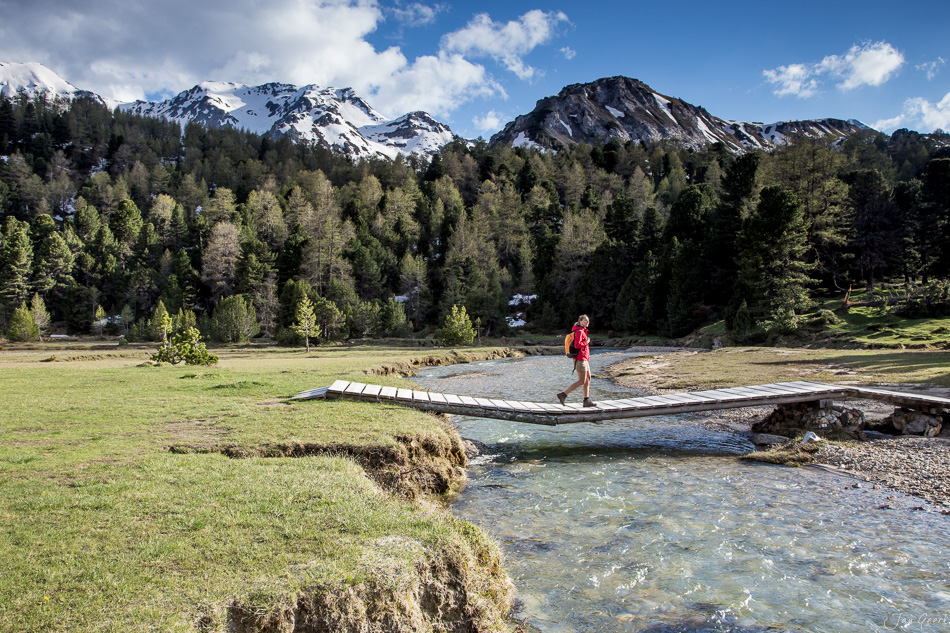 Wanderer auf Holzsteg über Fluss im Bleniotal mit schneebedeckten Bergen Tessin Schweiz Jan Geerk Fotograf Basel