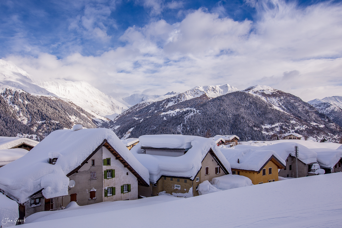 Schneebedeckte Häuser und Villen in Bedretto vor verschneiten Bergen und Alpenpanorama im Tessin Schweiz – Jan Geerk Fotograf Basel