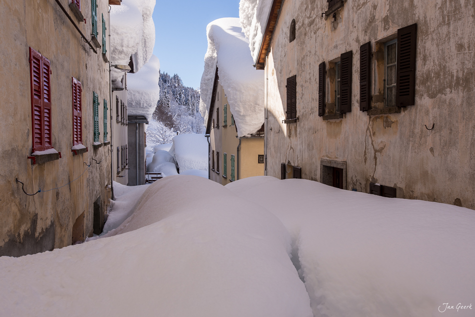 Verschneite Dorfstrasse in Bedretto mit traditionellen Tessiner Häusern im Winter – Jan Geerk Fotograf Basel