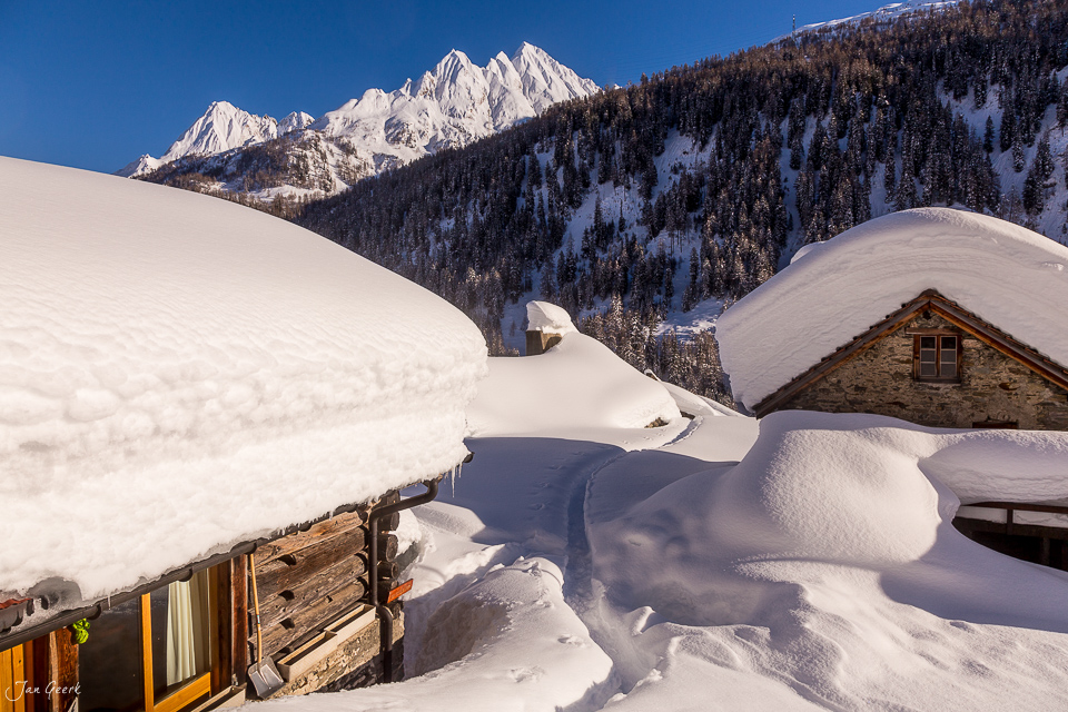 Schneebedeckte Steinhäuser und Berggipfel im Winter in Bedretto, Tessin, Schweiz – Jan Geerk Fotograf Basel