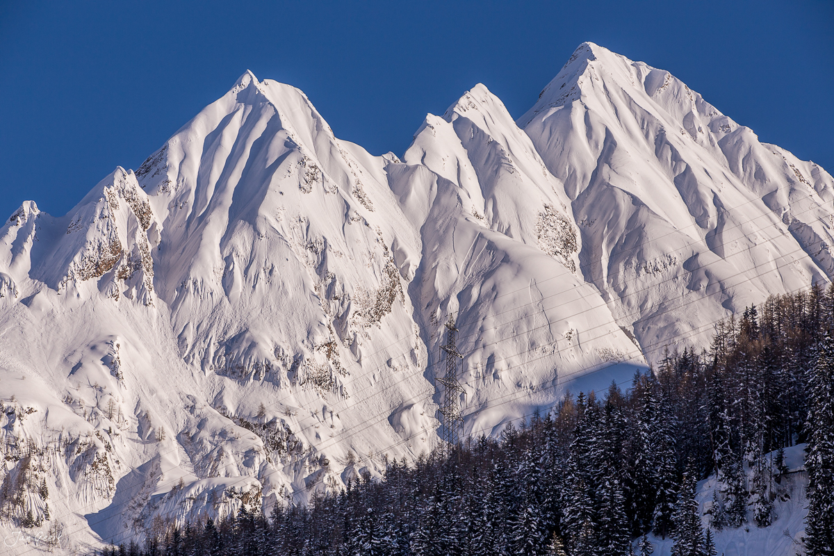Schneebedeckte Bergpipel mit Föhrenwäldern in Bedretto, Wintersonne über den Südalpen Tessin Schweiz – Jan Geerk Fotograf Basel