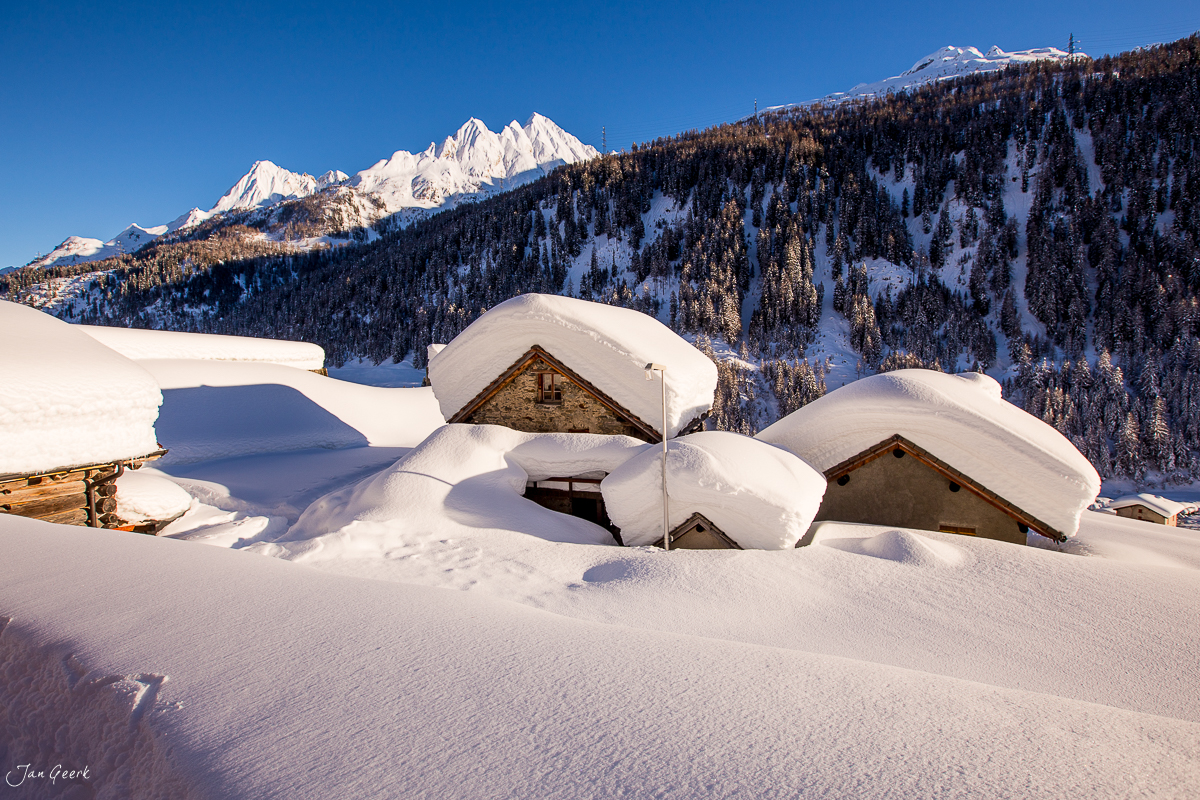 Schneebedeckte Alphütten in Bedretto mit verschneiten Südalpen im Hintergrund, Winterstimmung Tessin Schweiz – Jan Geerk Fotograf Basel