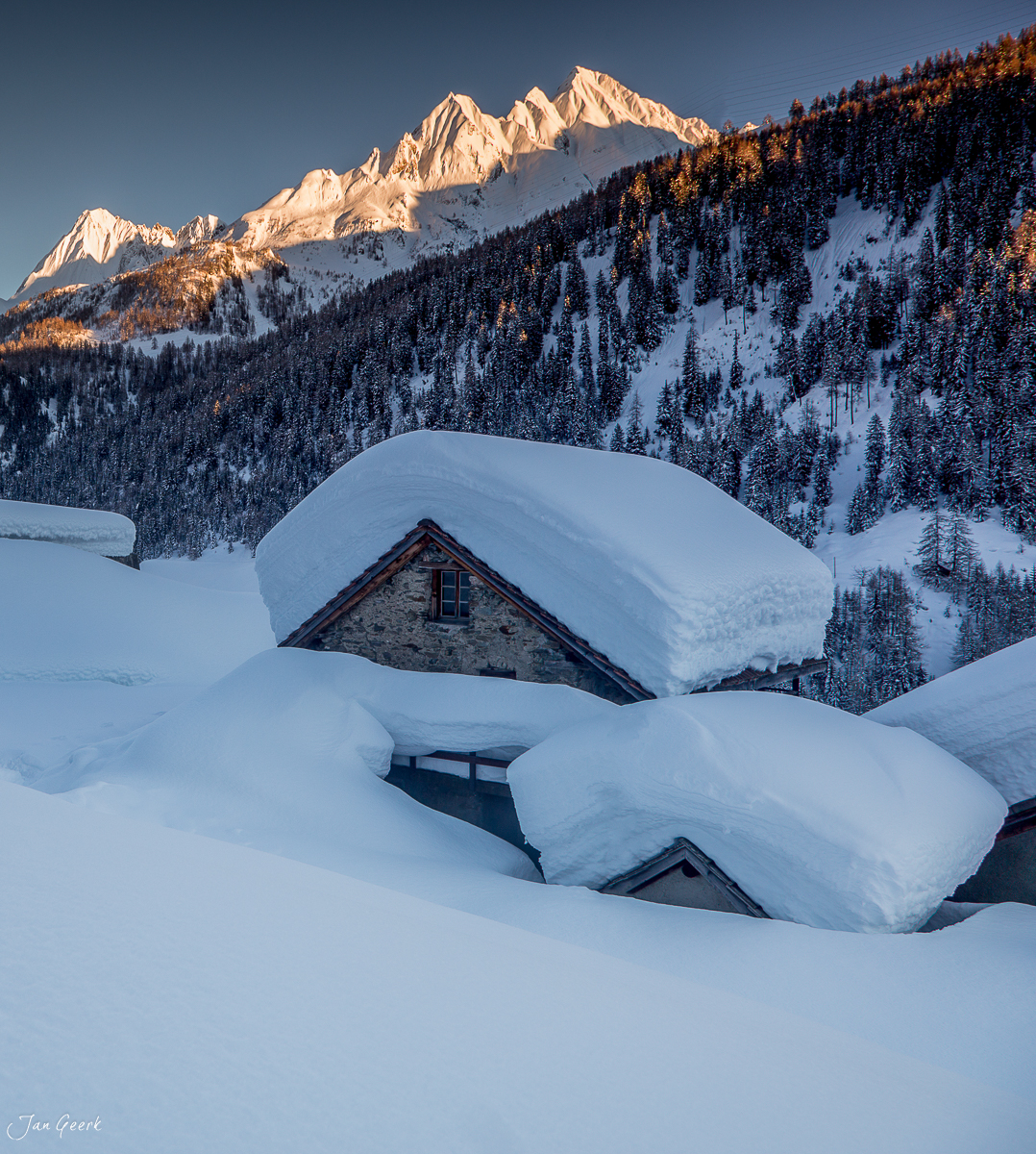 Schneebedeckte Alphütten in Bedretto im Tessin, verschneite Landschaft mit Bergen im Winterlicht, Schweiz – Jan Geerk Fotograf Basel