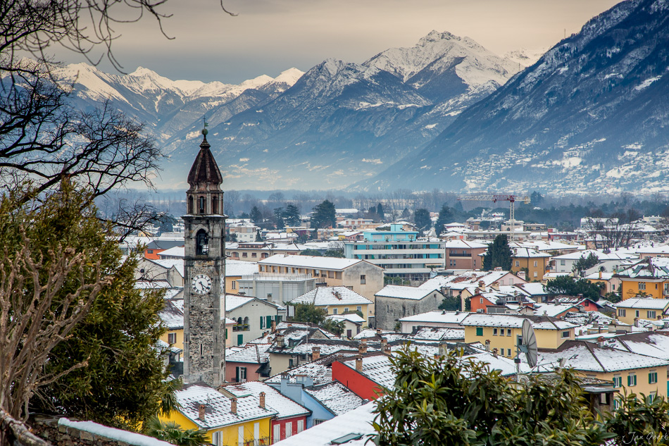 Winterliche Stadtansicht von Locarno mit schneebedeckten Dächern, Campanile und schneebedeckten Bergen im Hintergrund, Tessin Schweiz – Jan Geerk Fotograf Basel