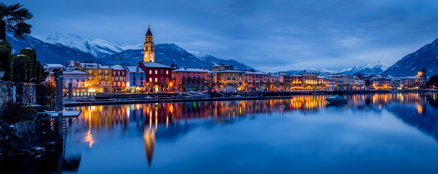 Ascona Hafen und Ufer mit beleuchteten Häusern, schneebedeckte Berge, Dämmerungsstimmung, Tessin Schweiz – Jan Geerk Fotograf Basel