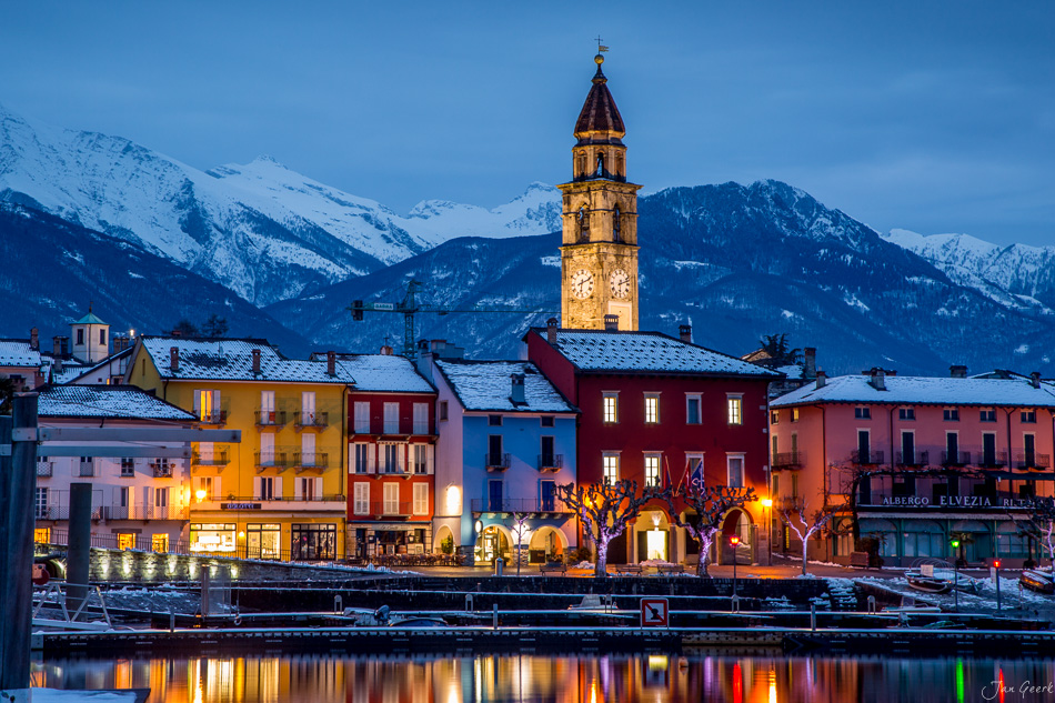 Ascona Seeufer bei Nacht mit Kirchturm, schneebedeckten Bergen und farbigen Häuserfassaden, Wintertag in Tessin Schweiz – Jan Geerk Fotograf Basel
