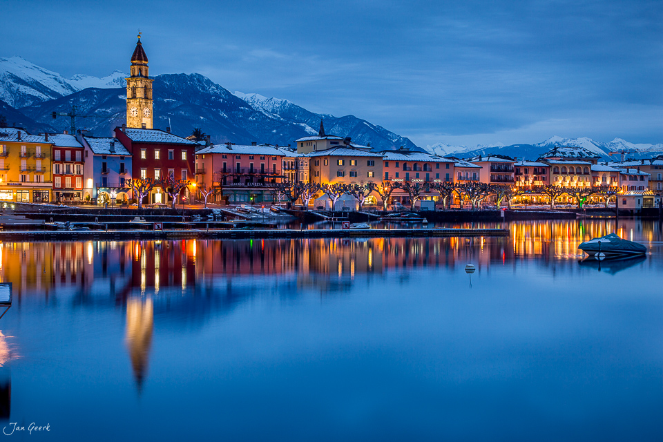 Ascona am Lago Maggiore mit beleuchteter Altstadt, schneebedeckten Bergen und winterlicher Abenddämmerung im Tessin Schweiz – Jan Geerk Fotograf Basel