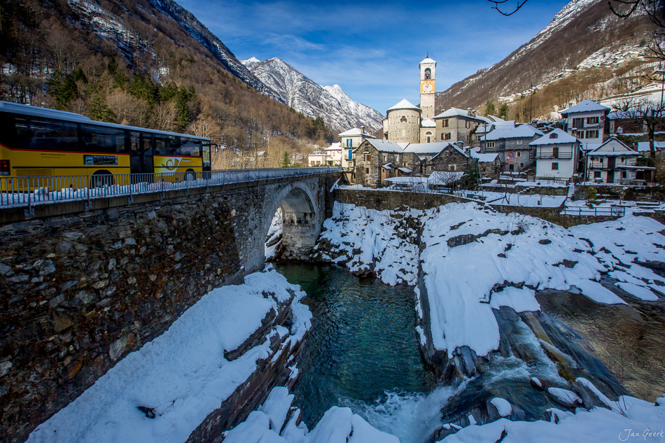 Verschneite Berglandschaft mit gelbem Postauto und Kirche in Locarno während Winterstimmung im Tessin Schweiz – Jan Geerk Fotograf Basel