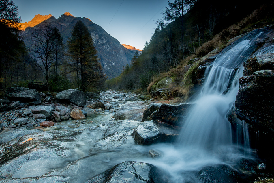 Wasserfall und Bergbach im Tessin mit Alpengipfel und Lärchenwald bei Sonnenaufgang, Schweiz – Jan Geerk Fotograf Basel