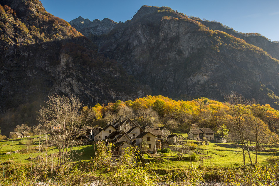 Herbstliche Berglandschaft mit traditionellen Steinhäusern im Tessin, golden beleuchtete Laubwälder und Felswände, Schweiz – Jan Geerk Fotograf Basel