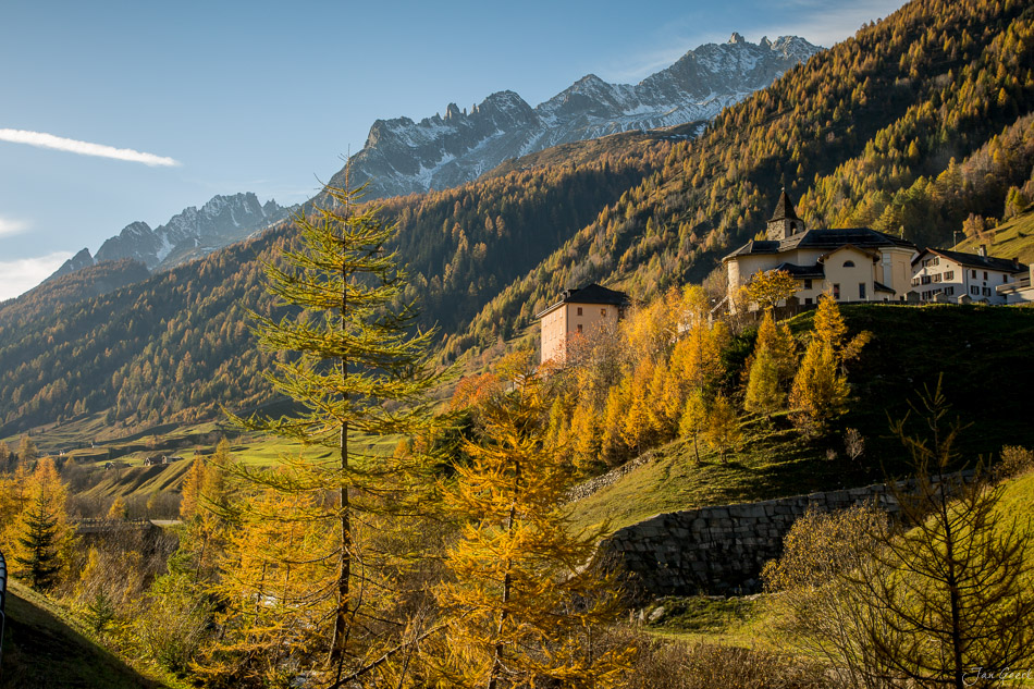 Herbstliche Berglandschaft im Tessin mit goldenem Lärchwald, Berggasthof und schneebedeckten Alpen, Schweiz – Jan Geerk Fotograf Basel