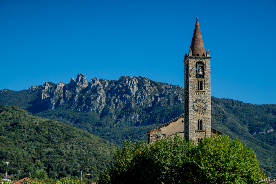 Kirche mit Glockenturm vor dramatischen Bergketten in Bellinzona, Tessin an sonnigem Sommertag – Jan Geerk Fotograf Basel