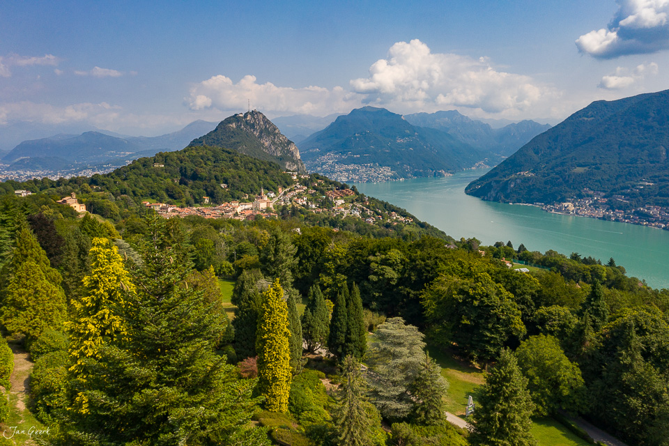 Luftaufnahme Tessin mit türkisblauem See, grünen Bergen und Dörfern unter Sommerwolken – Jan Geerk Fotograf Basel