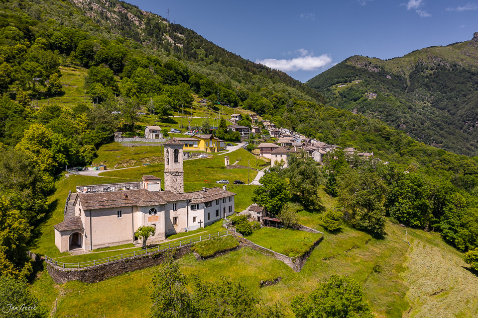 Luftaufnahme des Bergdorfes Indemini mit Steinkirche und traditionellen Rustici-Häusern im grünen Tessin, Sommerlicht, Schweiz – Jan Geerk Fotograf Basel