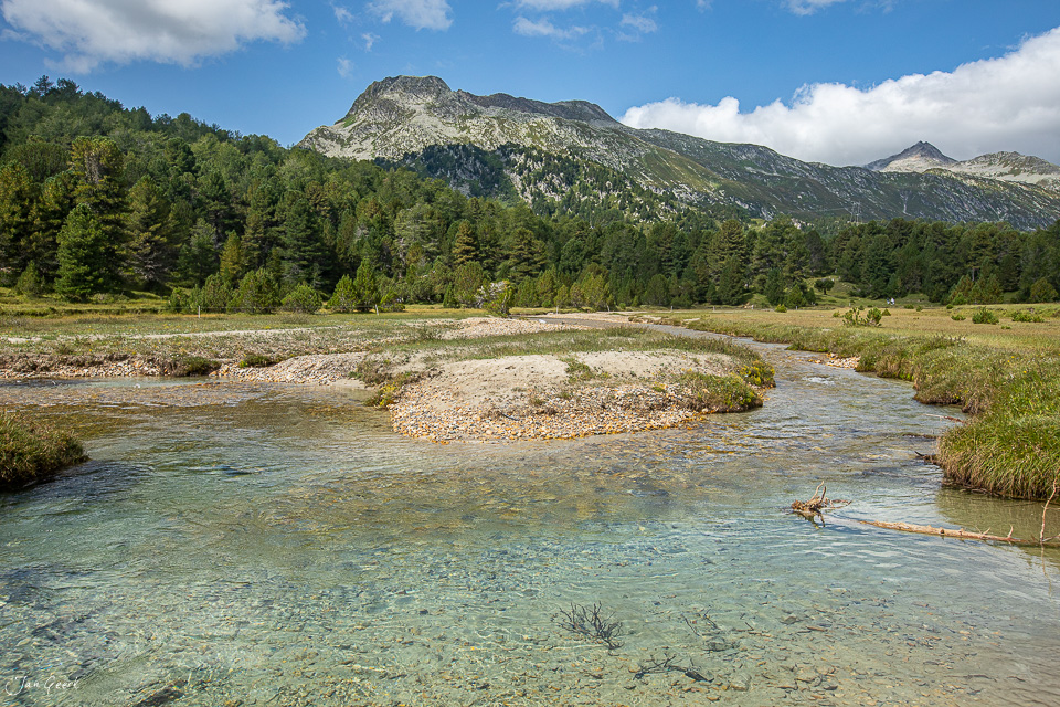 Kristallklarer Gebirgsfluss mit Kiesbänken, umgeben von Nadelwald und Alpengipfeln im Tessin, Sommerlicht – Jan Geerk Fotograf Basel