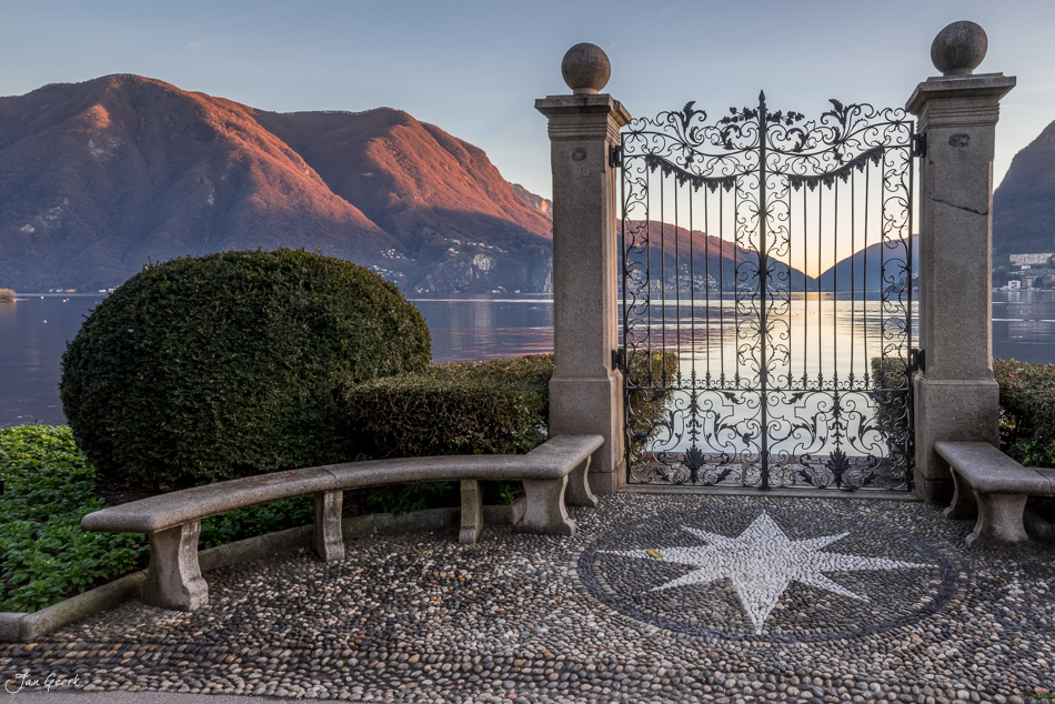 Verzierte Eisentor mit Seeblick auf Lugano, schneebedeckte Berge im Dezemberlicht, Tessin Schweiz – Jan Geerk Fotograf Basel