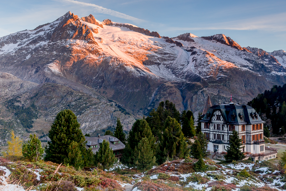 Herbstliches Aletschgebiet mit schneebedeckten Bergen und charakteristischem Chalet unter Lärchen Wallis Schweiz – Jan Geerk Fotograf Basel