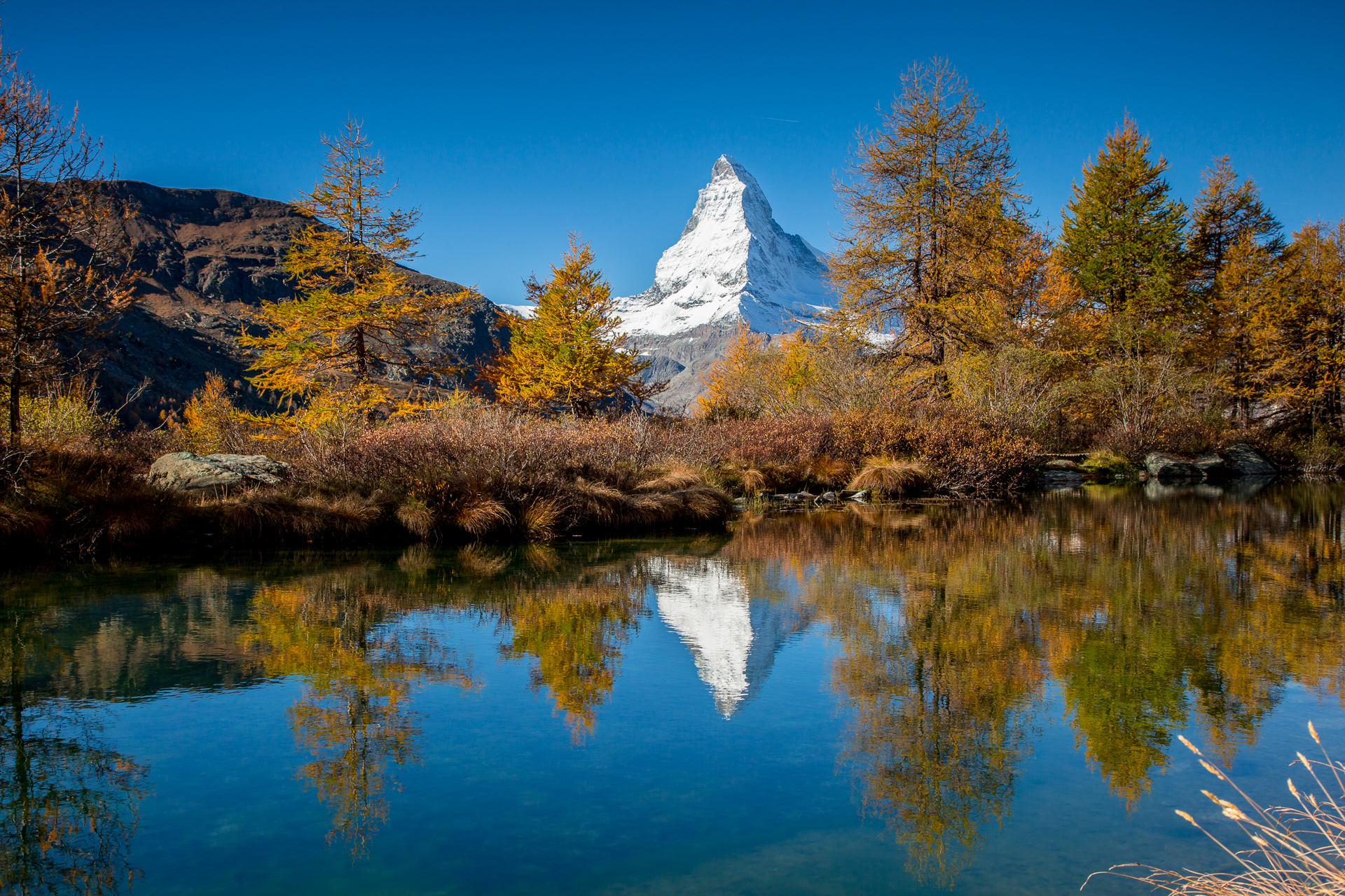 Spiegelglatter Bergsee mit schneebedecktem Matterhorn, Herbstlärchen in Gold, Wallis Schweiz – Jan Geerk Fotograf Basel