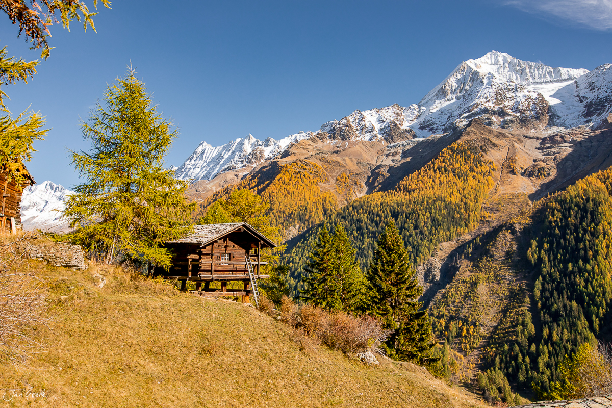 Berghütte mit Lärchen im Herbst im Lötschental, schneebedeckte Berge im Hintergrund, Wallis Schweiz – Jan Geerk Fotograf Basel