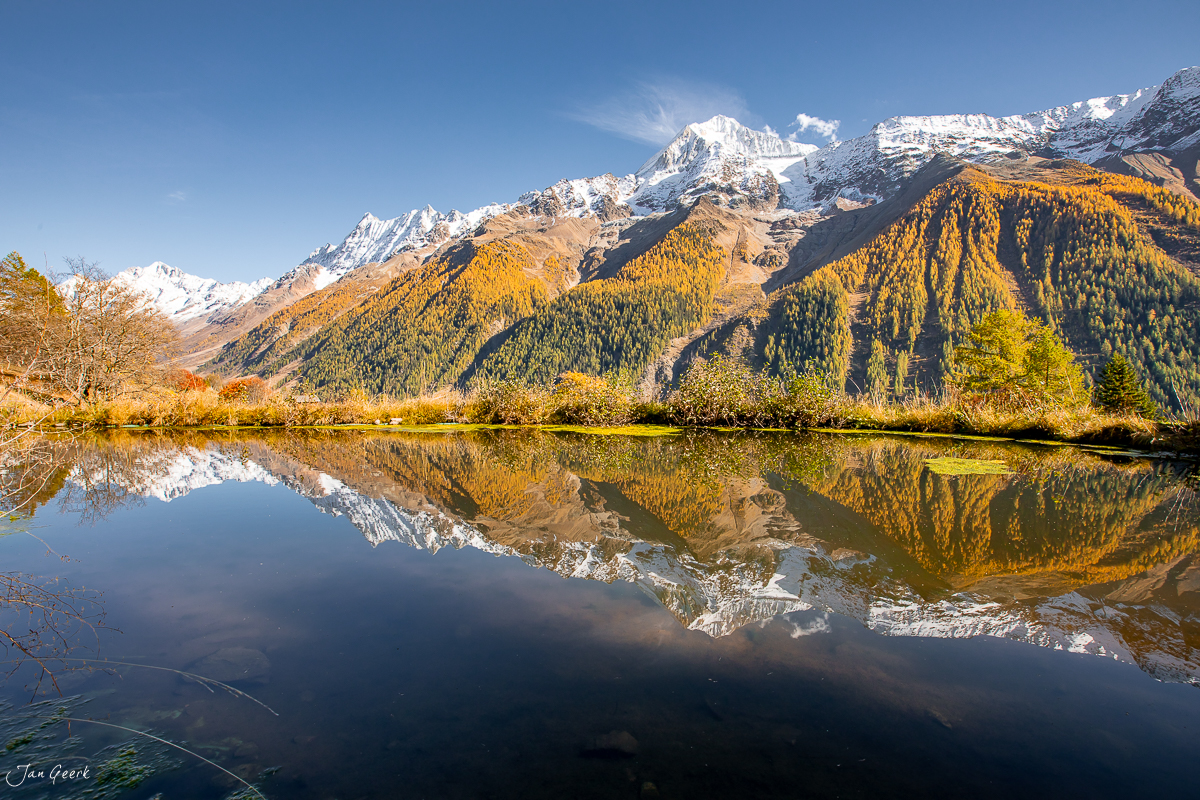 Spiegelglatter Bergsee im Lötschental mit schneebedeckten Gipfeln, goldenen Herbstlärchen und klarem Himmel – Wallis Schweiz Jan Geerk Fotograf Basel