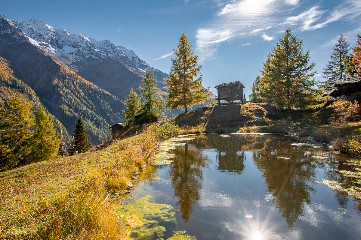 Herbstliche Berglandschaft am Grundsee im Lötschental mit goldenen Lärchen, schneebedeckten Gipfeln und Spiegelbild im Wasser – Jan Geerk Fotograf Basel Schweiz