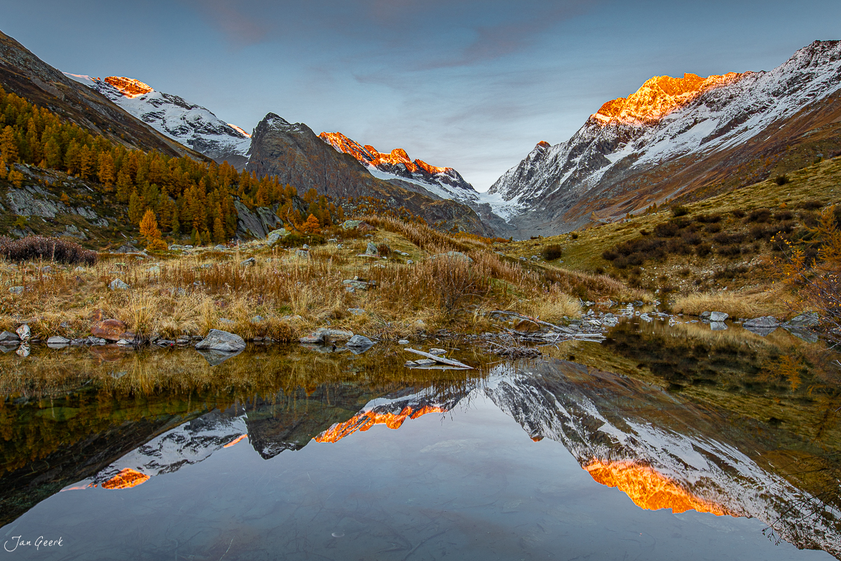 Spiegelung eines Bergsees im Lötschental mit schneebedeckten Gipfeln und goldener Herbstlärchen Wallis Schweiz Jan Geerk Fotograf Basel