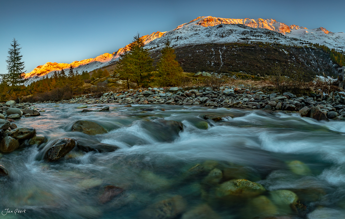 Bergfluss mit Steinen im Lötschental, schneebedeckte Berggipfel in Herbstlicht, Wallis Schweiz – Jan Geerk Fotograf Basel