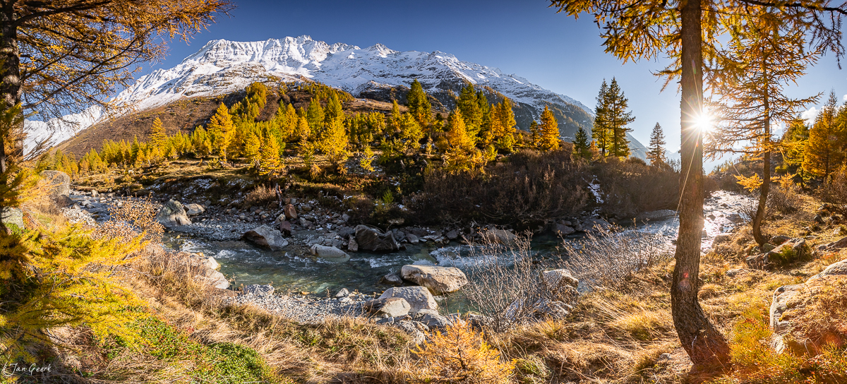Herbstliche Lärchen am Bach mit schneebedecktem Berg im Lötschental Wallis Schweiz – Jan Geerk Fotograf Basel