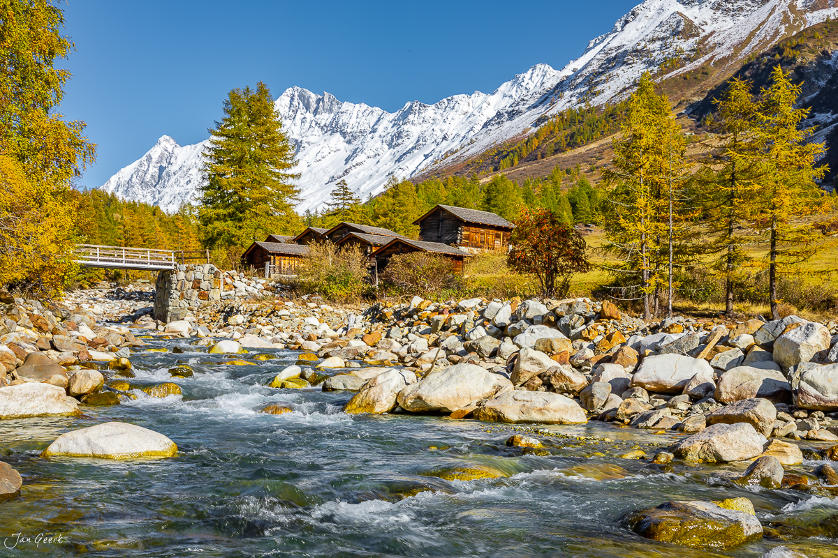 Bergbach mit Steinen, Alphütten und schneebedeckte Berge im Herbst im Lötschental Wallis Schweiz – Jan Geerk Fotograf Basel