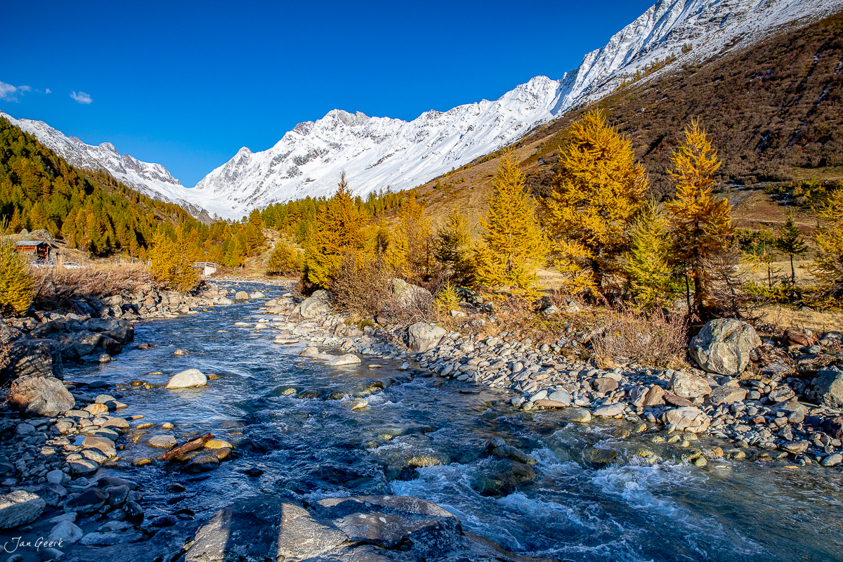 Gebirgsbach mit Herbstlärchen im Lötschental, schneebedeckte Gipfel, goldenes Licht, Wallis Schweiz – Jan Geerk Fotograf Basel