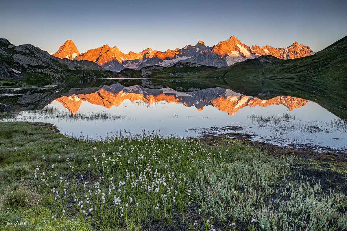 Bergsee mit weißem Wollgras und schneebedeckten Bergspitzen im Alpenglow während goldener Sommerstunde Wallis Schweiz – Jan Geerk Fotograf Basel