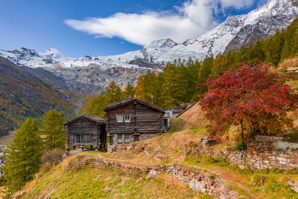 Holzhütten mit rotem Herbstlaub vor schneebedeckten Alpen in der Aletschregion Wallis Schweiz – Jan Geerk Fotograf Basel