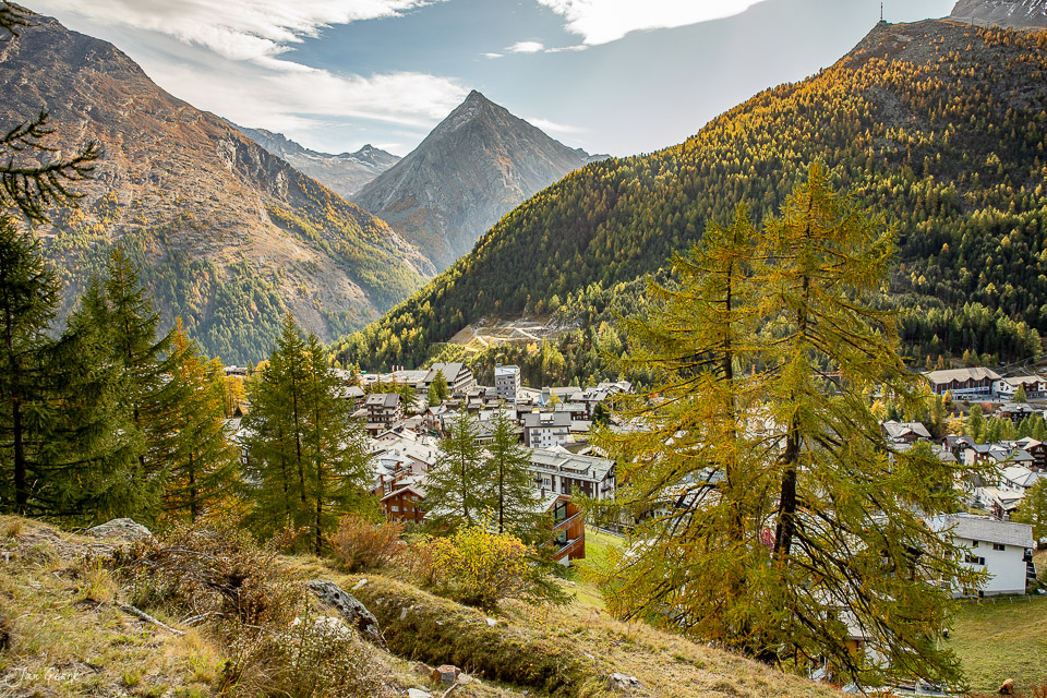 Herbstliche Berglandschaft in Riederalp mit goldenem Lärchenwald, pyramidenförmigen Bergen und Dorfsilhouette im Wallis, Schweiz – Jan Geerk Fotograf Basel